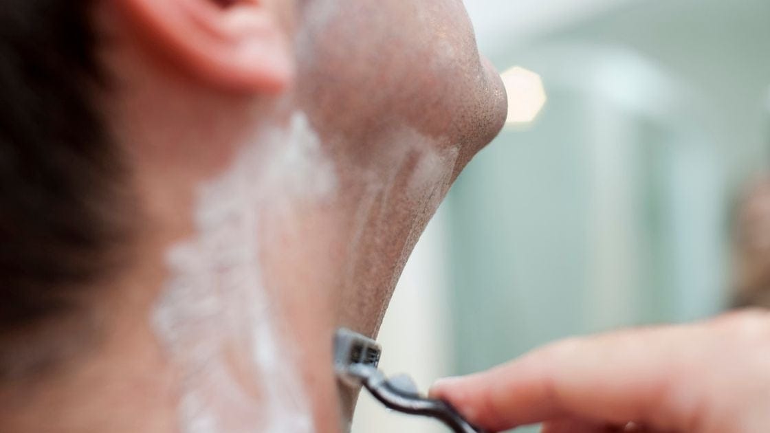 A man is shaving his neck with an electric razor.