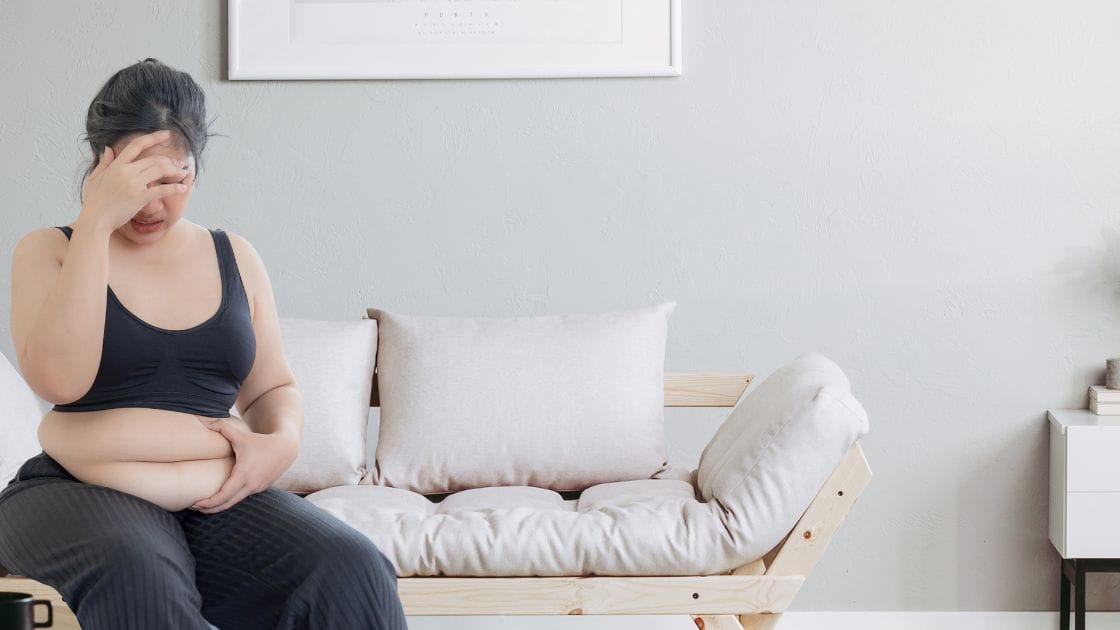 A woman is sitting on a couch with her hands on her stomach.