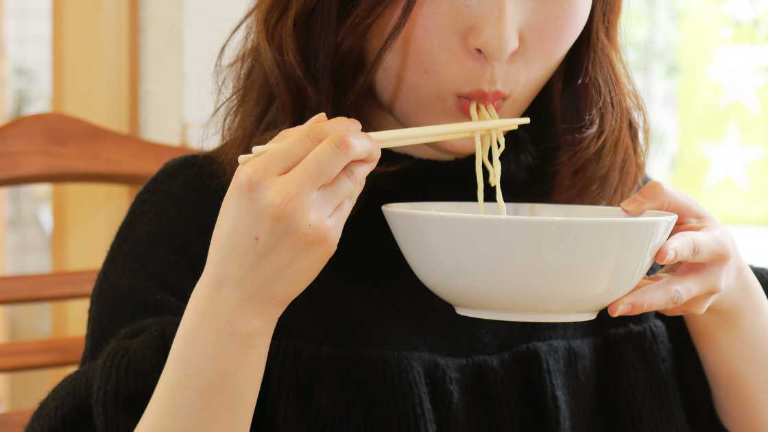 A woman is eating noodles from a bowl.
