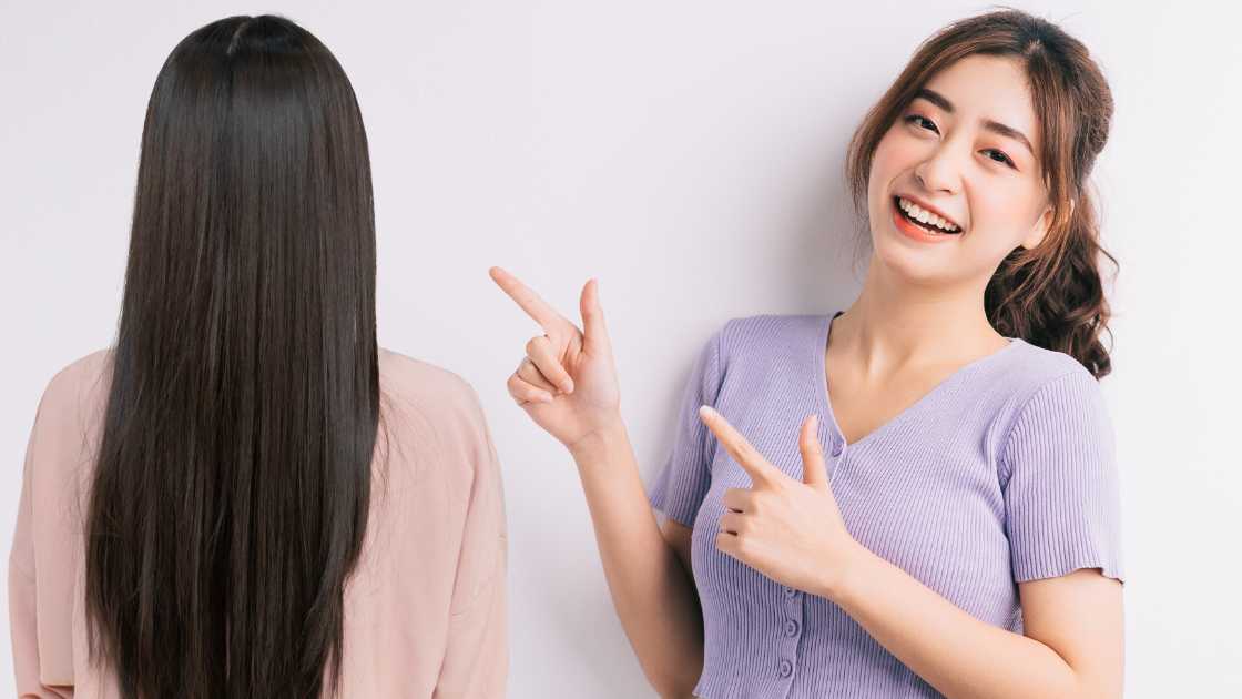 Two women with long hair pointing at each other.