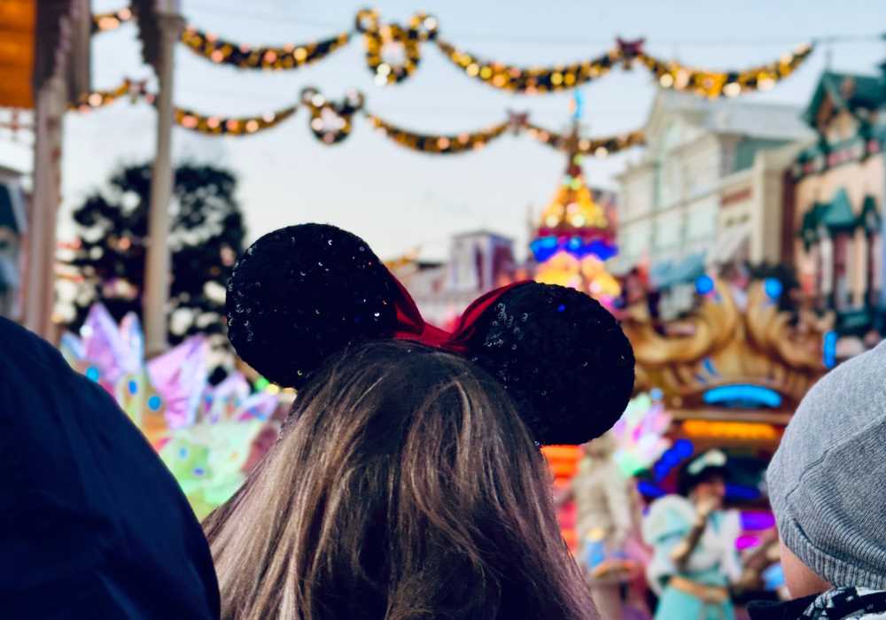 Person wearing mickey mouse ears at a festive street parade.
