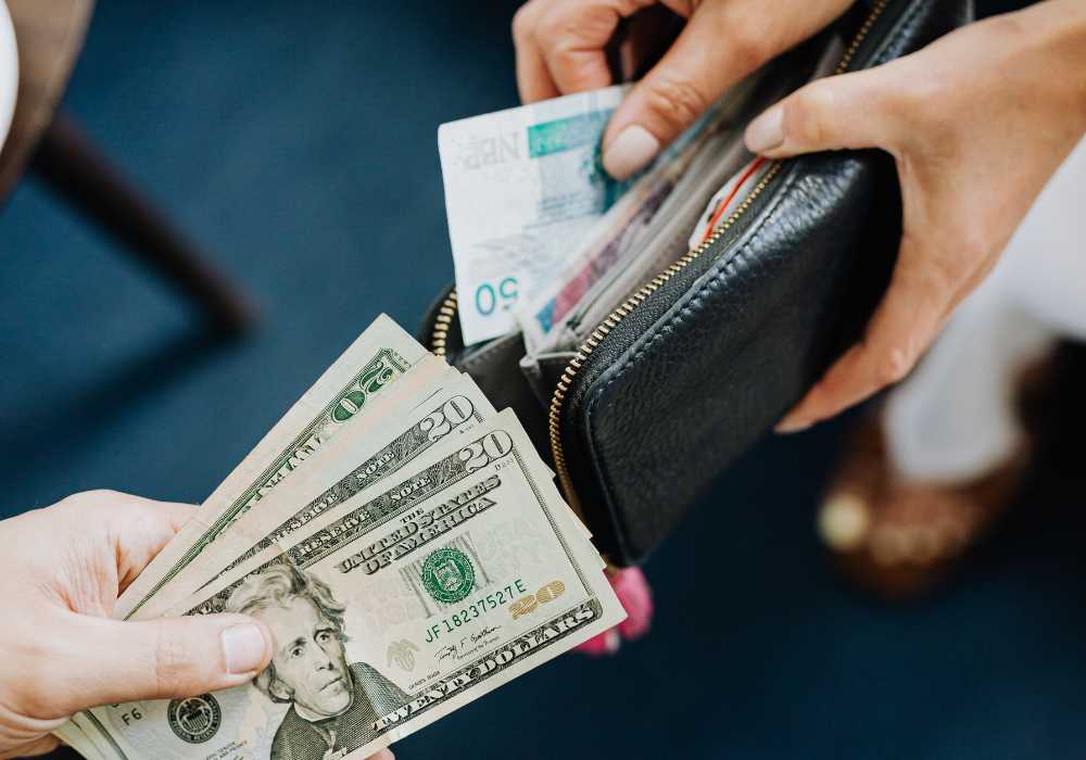 A woman handing money to another person in a black wallet.
