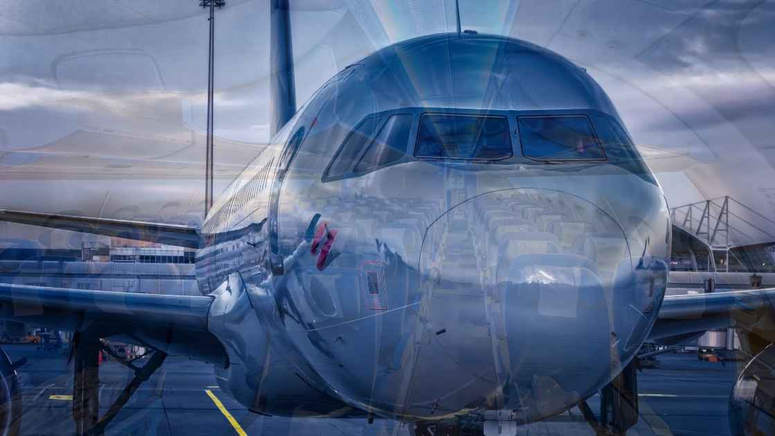 A commercial airliner parked at a gate under a cloudy sky, with visible reflections on its shiny blue fuselage.