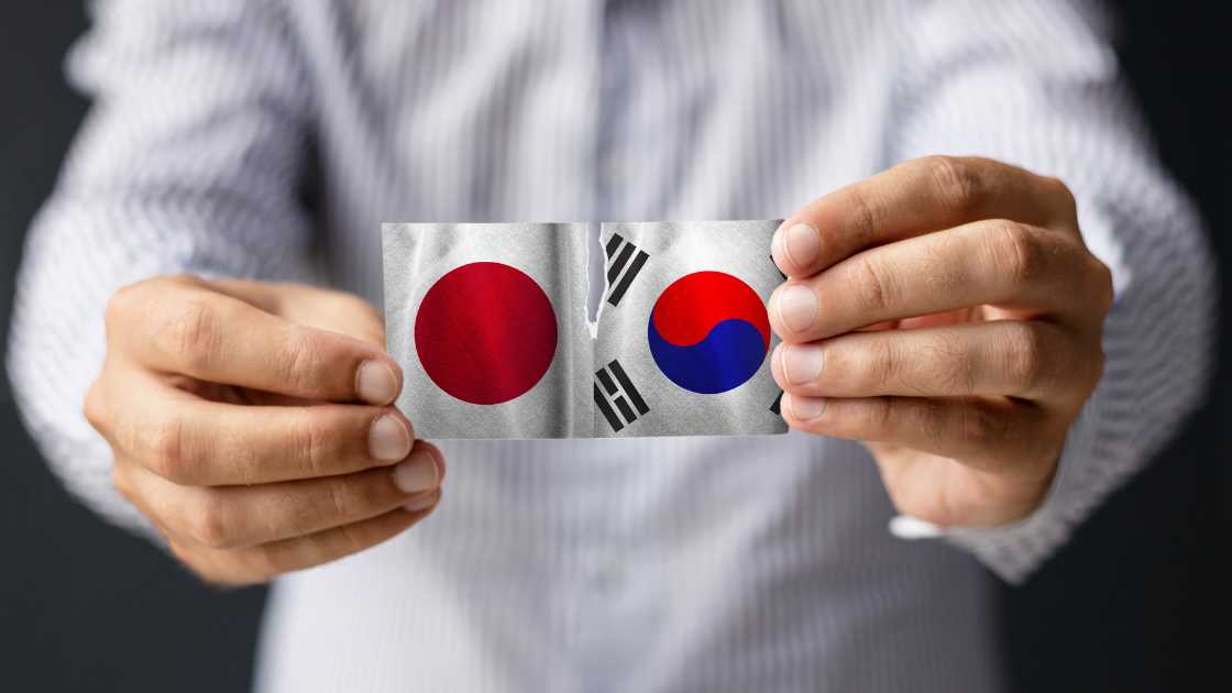 A person holding a torn paper showing the japanese and south korean flags, symbolizing strained relations between the two nations.