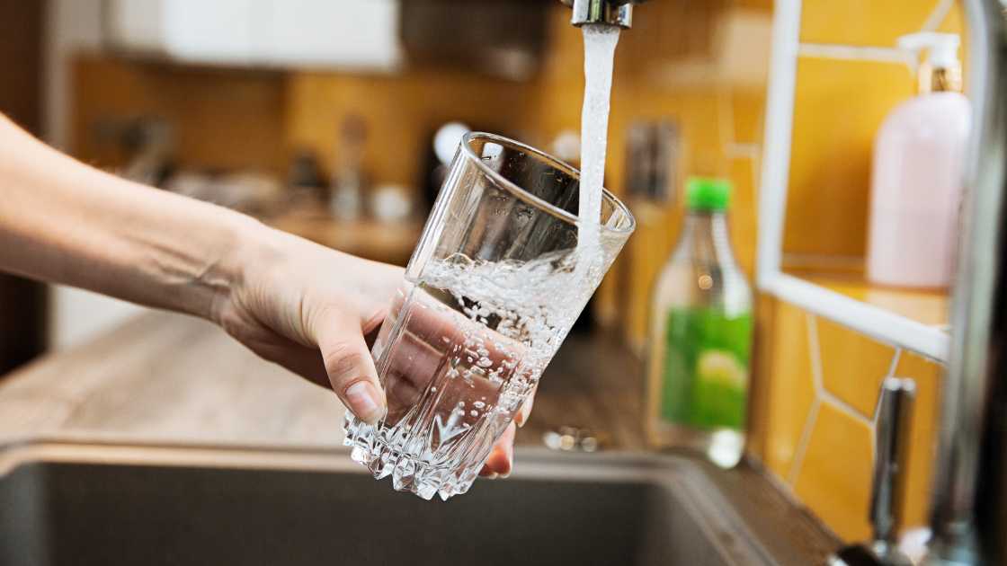 Person filling a glass with water from a kitchen faucet.