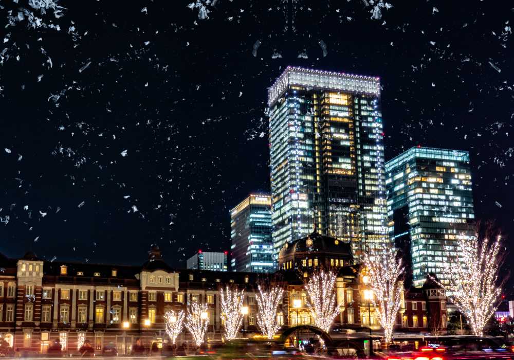 Nighttime cityscape featuring illuminated skyscrapers and decorated trees in the foreground, with a clear starry sky above.