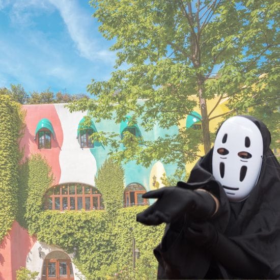 A person in a mask and costume stands in front of a colorful, ivy-covered building with arched windows and lush greenery.