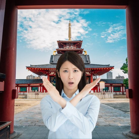 A woman standing in front of a traditional Japanese temple makes an 'X' shape with her arms, indicating disapproval or prohibition. The sky is clear with some scattered clouds.