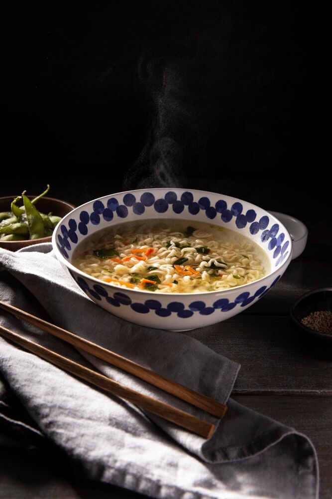 A bowl of Japanese soup with noodles, a raw egg yolk, chopped green onions, and vegetables, with text reading "7 Healthy Japanese Soups" and "japanwhisper.com".