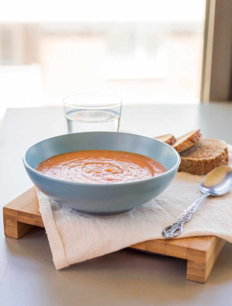 Person holding a bowl of soup with tofu, greens, and mushrooms in a modern kitchen setting.