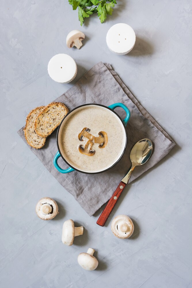 A black bowl of miso soup with three large mushrooms and chopped green onions, placed on a wooden surface.