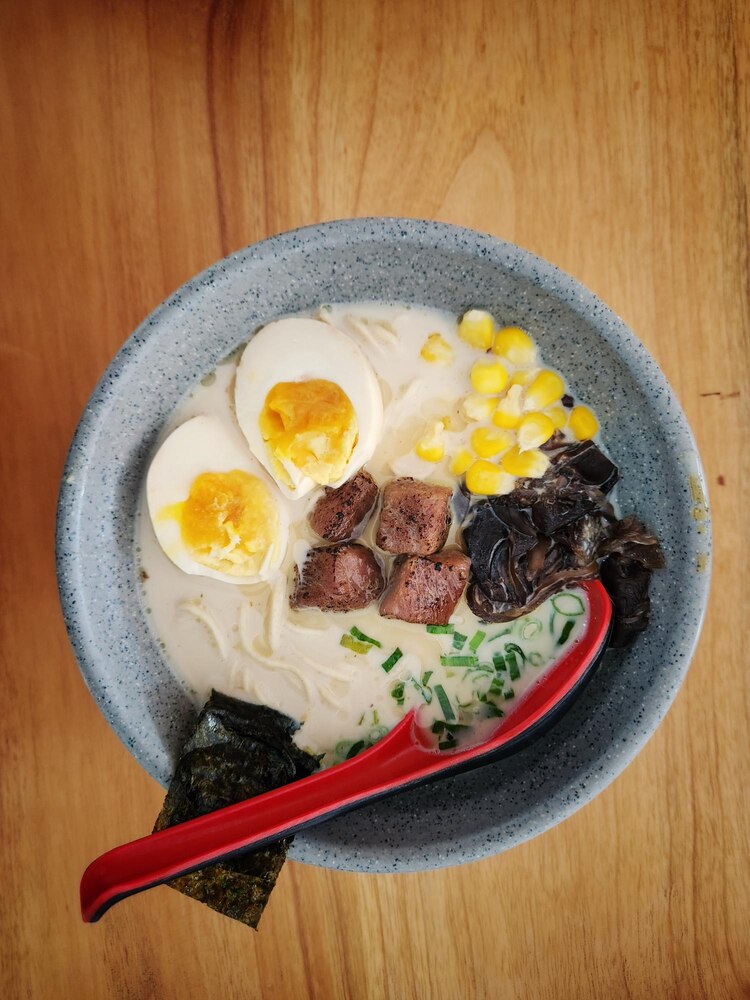 A bowl of clear soup with tofu cubes, a raw egg yolk, seaweed pieces, and sliced green onions, with a small flag labeled "japanwhisper.com.