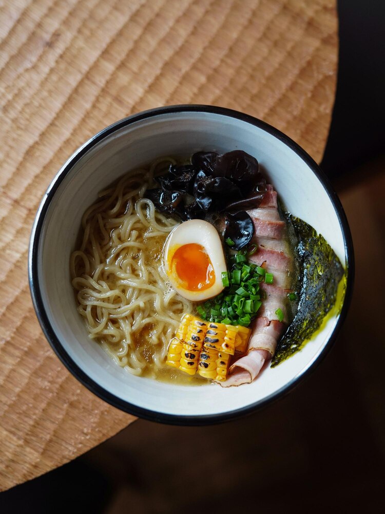 A bowl of ramen topped with sliced pork, radish, green onion, and seaweed, placed beside chopsticks and a ceramic chopstick rest on a green surface.