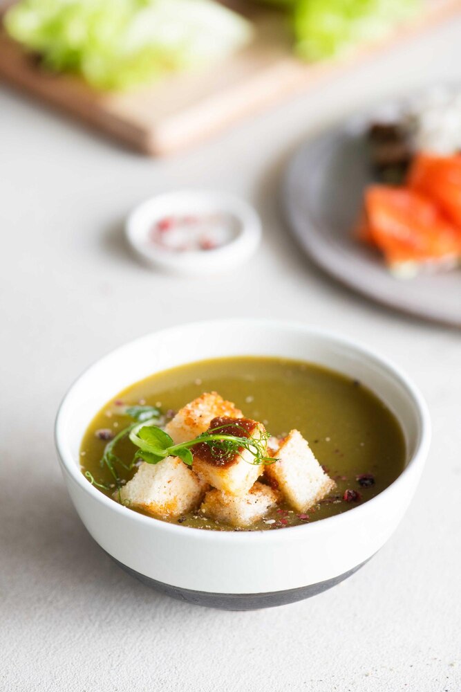 A bowl of miso soup with tofu and seaweed sits on a tray with chopsticks, set against a backdrop of a painted river and mountains.